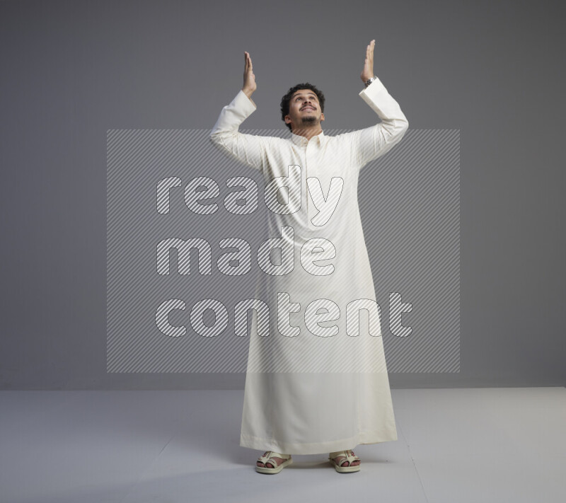 A Saudi man standing wearing thob interacting with the camera on gray background