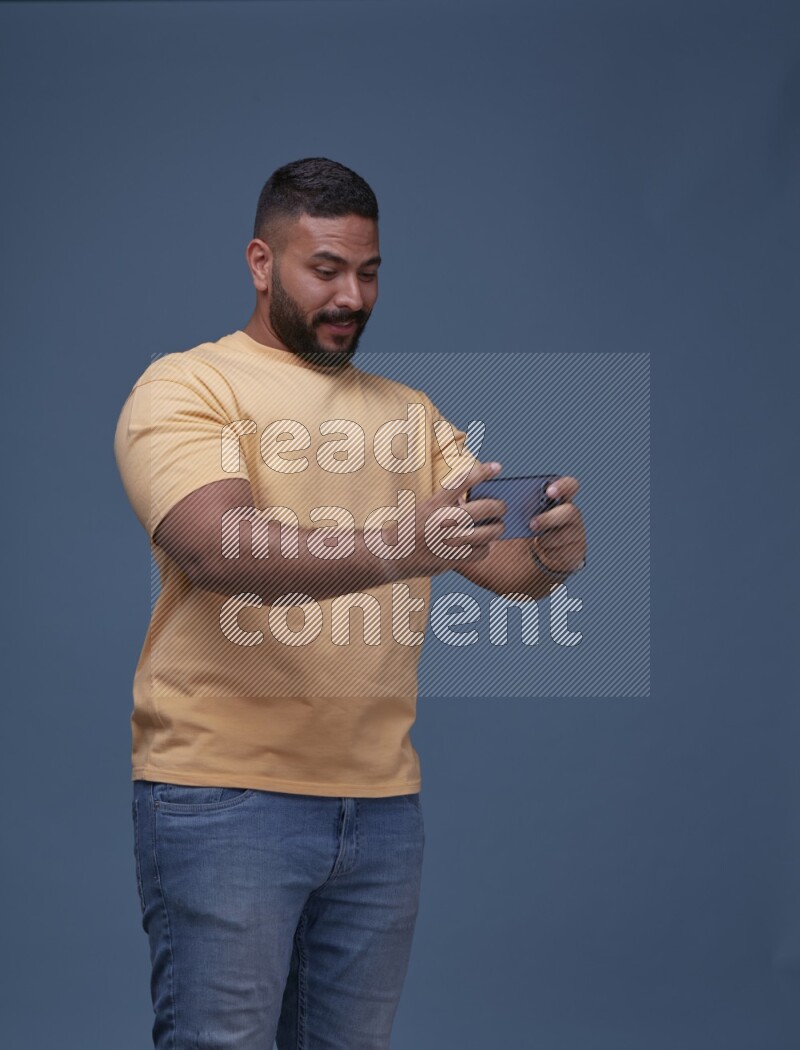 A man Playing Games on Smartphone on Blue Background wearing Orange T-shirt