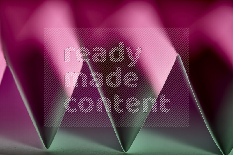 صورة مجردة مقربة تظهر طيات ورقية هندسية حادة بتدرجات اللون الأخضر والارجواني