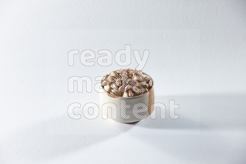 A beige ceramic bowl full of peeled pistachios on a white background in different angles