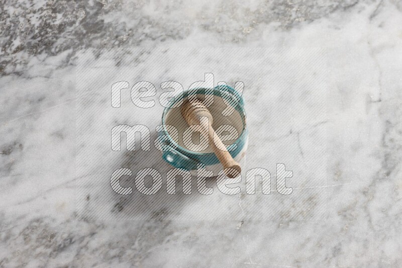 Multicolored pottery bowl with wooden honey dipper in it on grey marble background