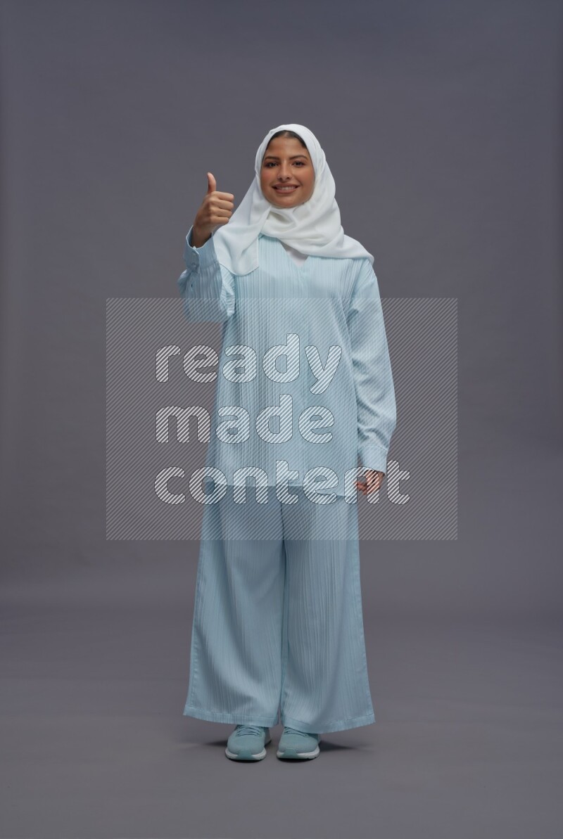 Saudi woman wearing hijab clothes standing interacting with the camera on gray background
