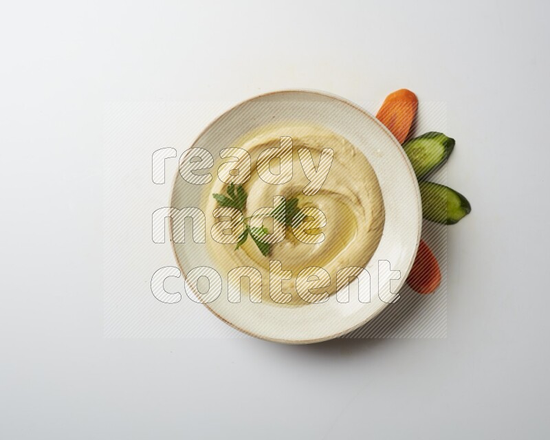 Hummus in a pottry plate garnished with parsley on a white back ground