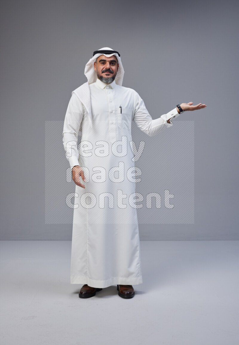 Saudi man Wearing Thob and white Shomag standing interacting with the camera on Gray background
