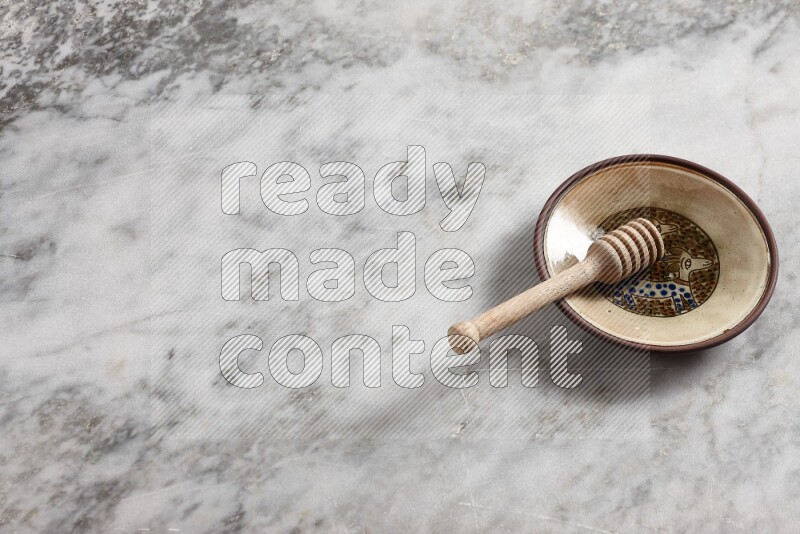 Decorative pottery plate with wooden honey dipper in it on grey marble background