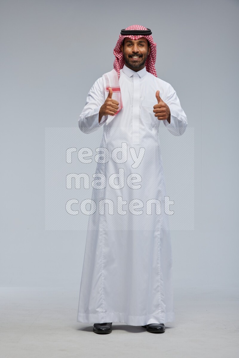 Saudi man Wearing Thob and shomag standing interacting with the camera on Gray background