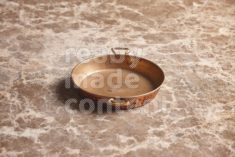 A small copper pan on beige marble background