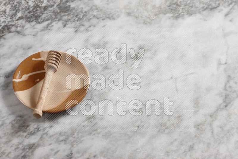Multicolored pottery plate with wooden honey dipper in it on grey marble background