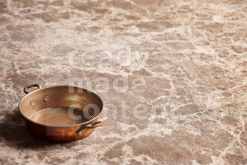 A small copper pan on beige marble background
