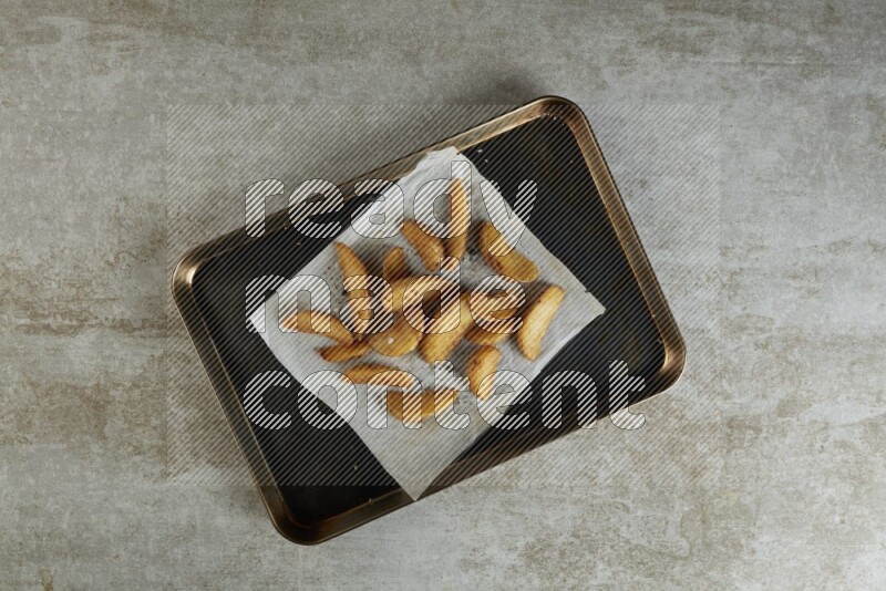 wedges potato on parchment paper in a black stainless steel rectangle tray on grey textured counter top