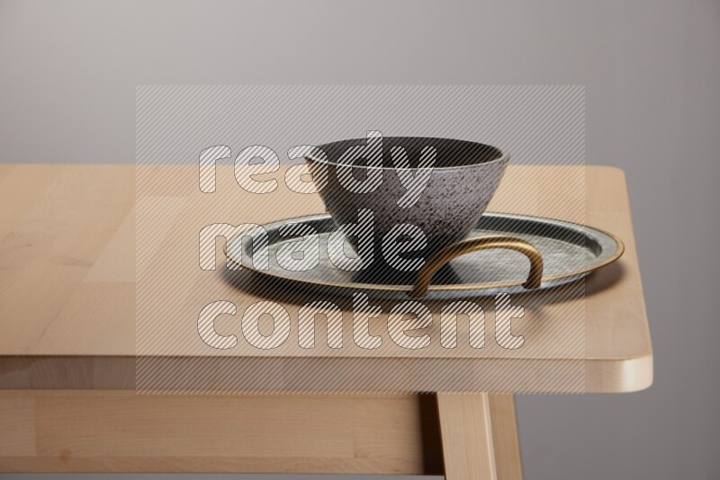 multicolored bowl placed on a rounded stainless steel tray with golden handels on the edge of wooden table