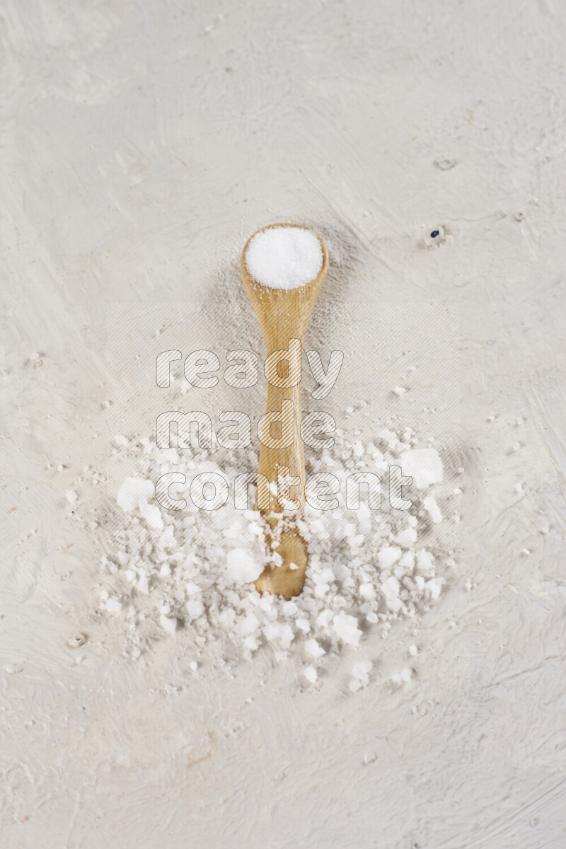 A wooden spoon full of white salt on white background