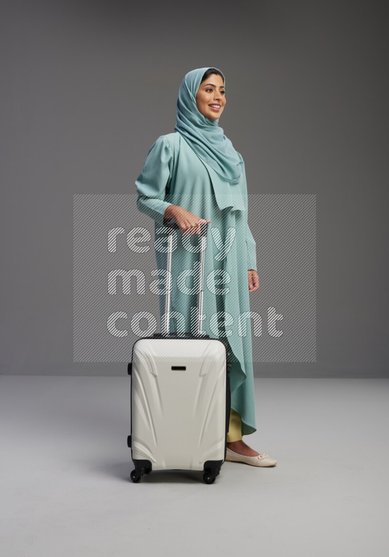 Saudi Woman wearing Abaya standing holding Travel bag on Gray background