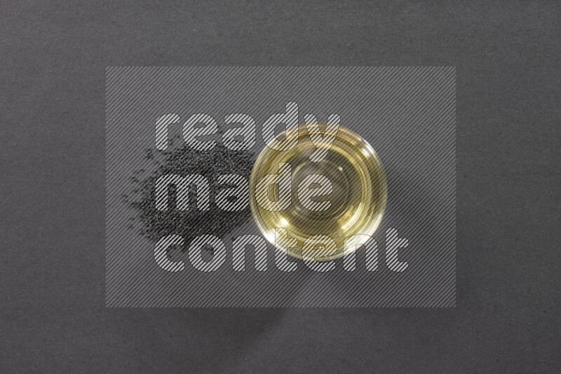 وعاء زجاجي ممتلئ بزيت حبة البركة مع بعض البذور بجانبه على أرضية سوداء