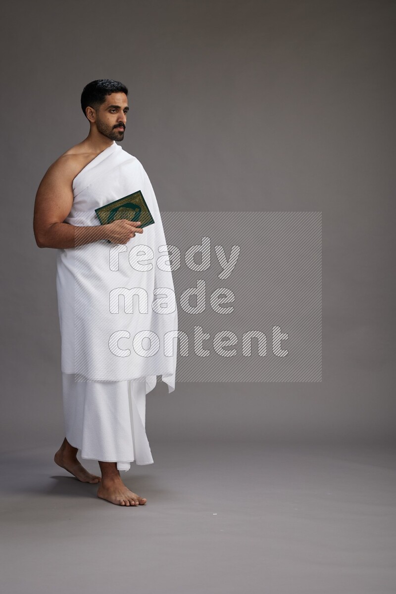 A man wearing Ehram Standing reading quran on gray background