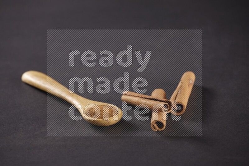 3 Cinnamon sticks stacked beside a wooden spoon full of cinnamon powder on black background in different angles