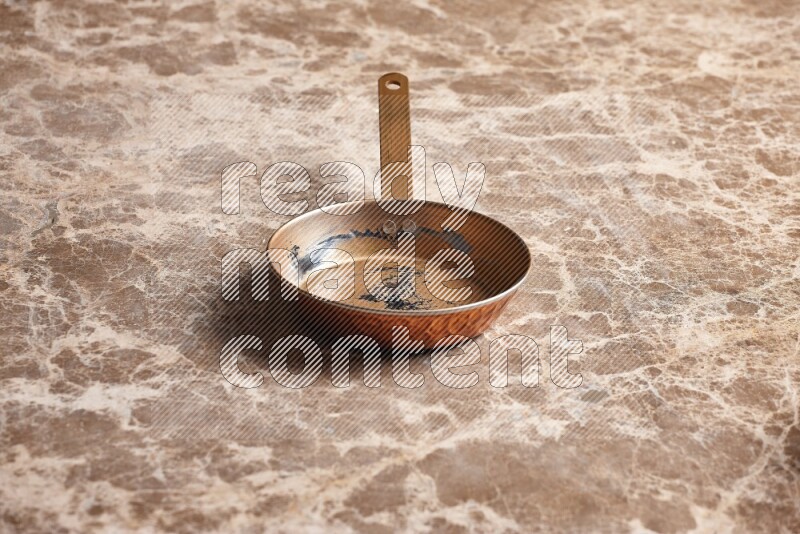 A small copper pan on beige marble background
