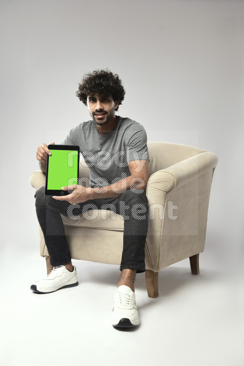 A man wearing casual sitting on a chair showing a tablet screen on white background