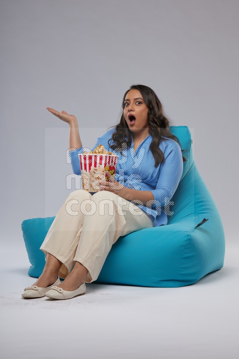 A woman sitting on a blue beanbag and eating popcorn