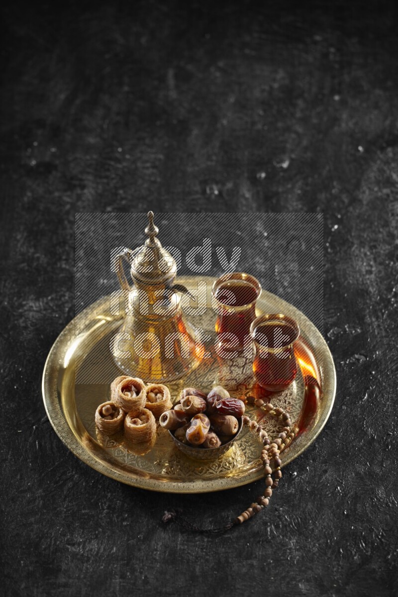 Oriental sweets with dates and a drink on a metal tray in a dark setup