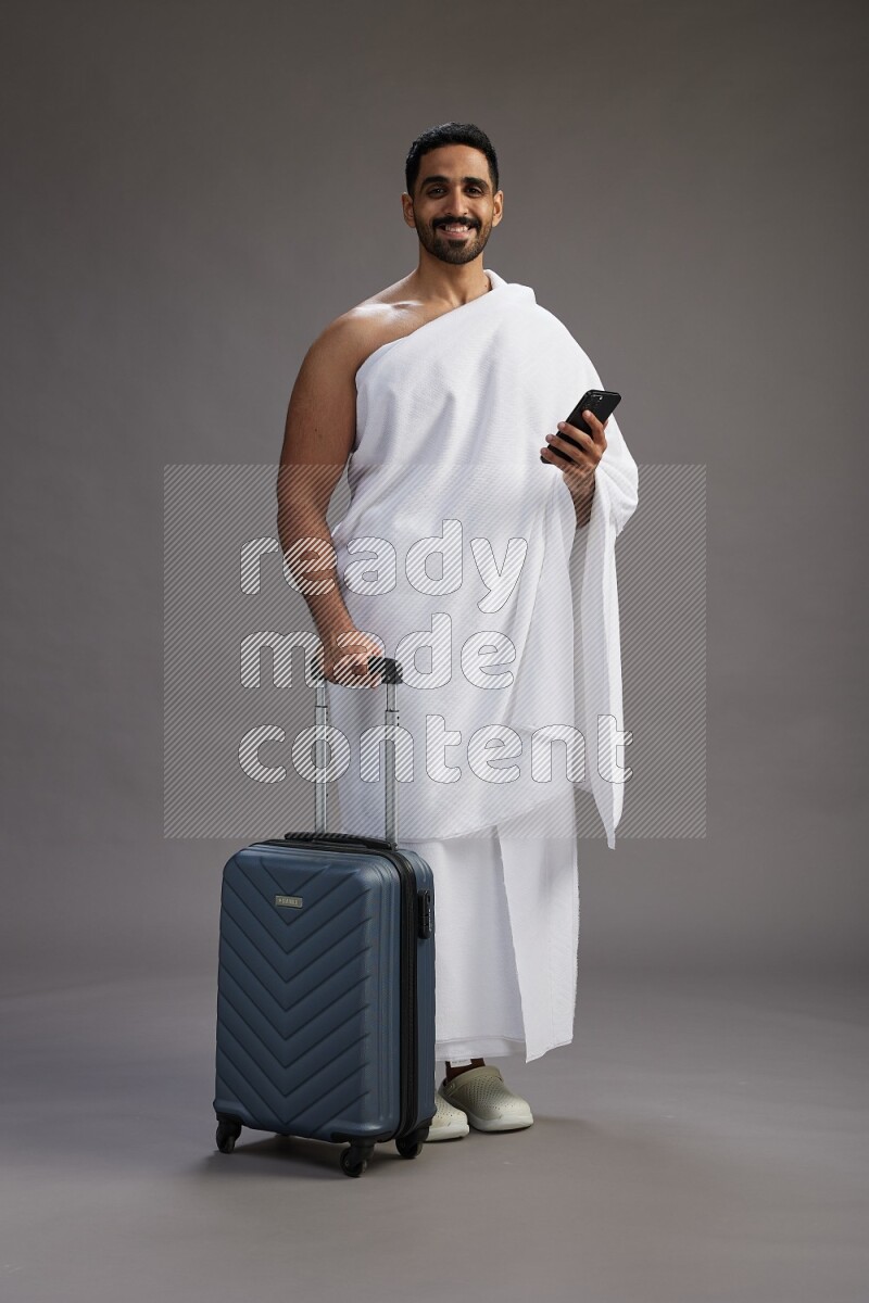 A man wearing Ehram Standing holding traveling bag on gray background