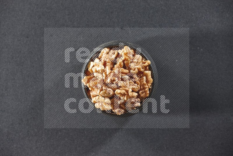 A black pottery bowl full of peeled walnuts on a black background in different angles
