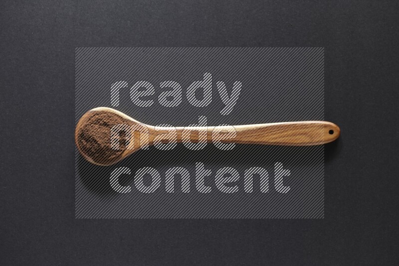 A wooden ladle full of cloves powder on a black flooring