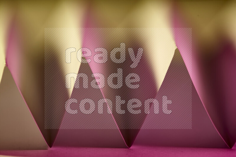 A close-up abstract image showing sharp geometric paper folds in pink gradients and warm tones
