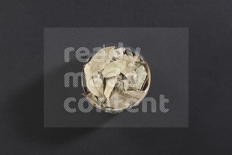 وعاء فخاري متعدد الألوان ممتلئ بأوراق الغار المجففة على أرضية سوداء