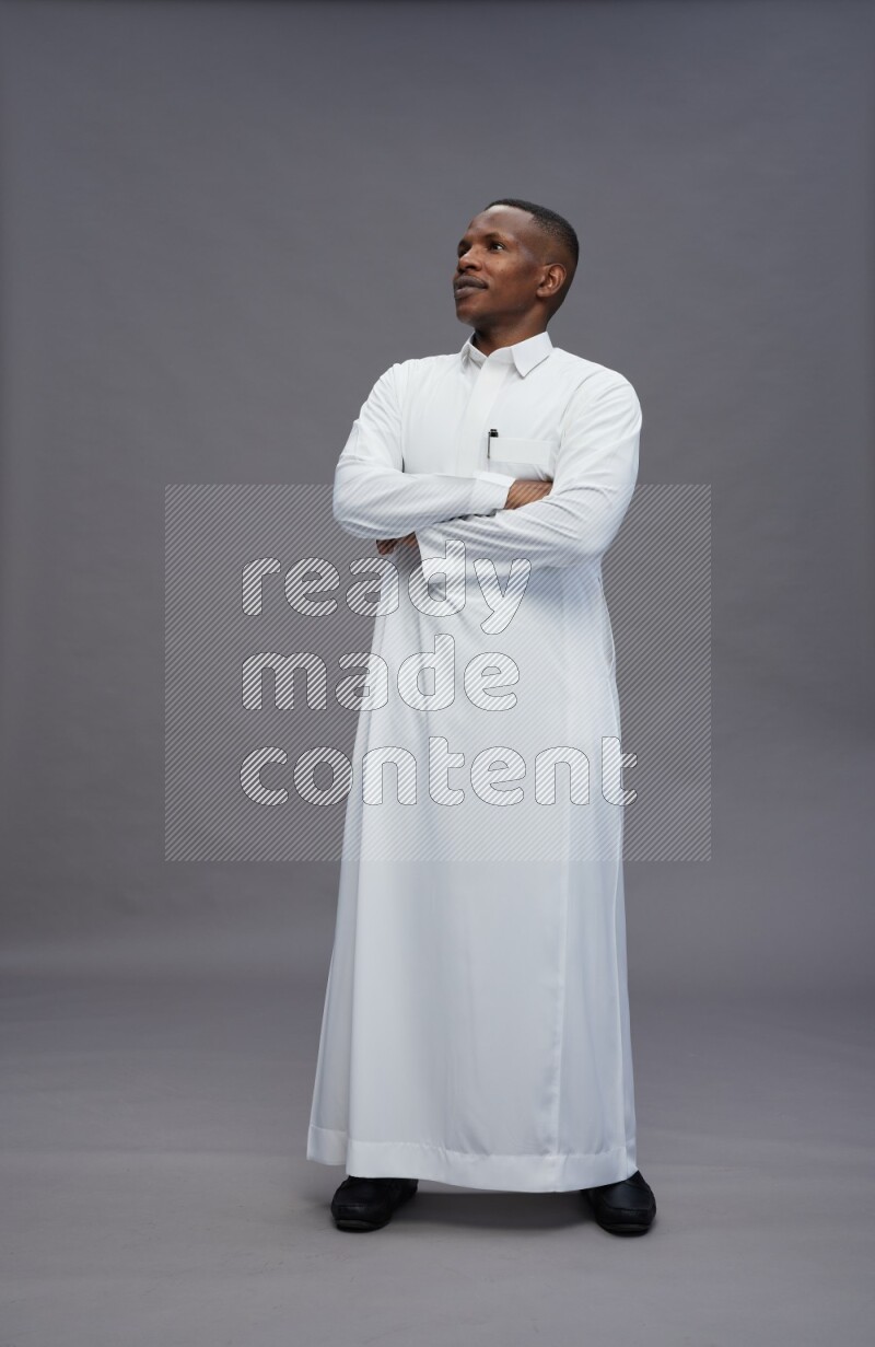 Saudi man wearing thob standing with crossed arms on gray background