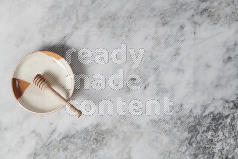 Multicolored pottery plate with wooden honey dipper in it on grey marble background