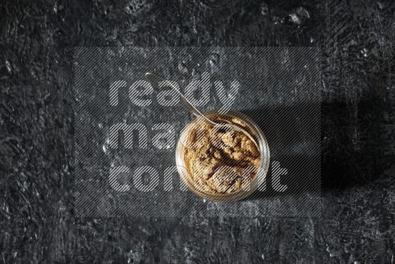 وعاء زجاجي للتوابل وملعقة معدنية ممتلئان ببودرة بهار الفلفل الحلو على خلفية سوداء