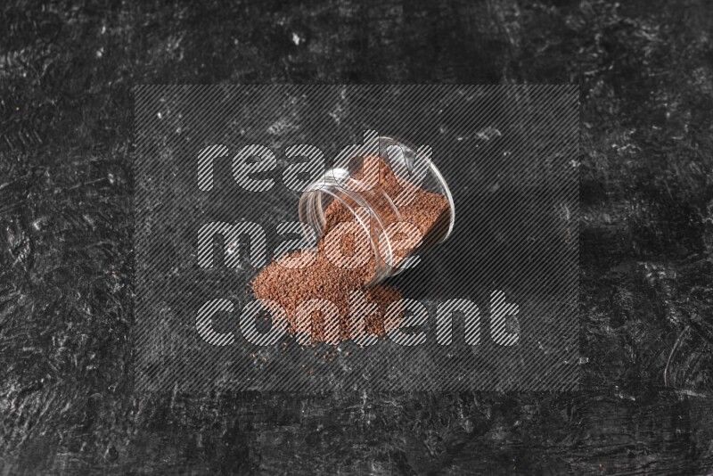 وعاء زجاجي مقلوب ممتلئ ببذور حب الرشاد وتناثرت البذور منه على أرضية سوداء