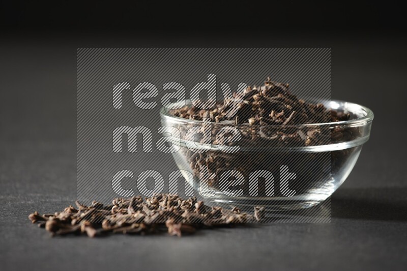 A glass bowl full of cloves on a black flooring