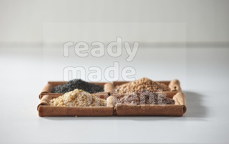 4 مربعات من أعواد القرفة ممتلئة بحبة البركة وبذور الخردل وبذور الكتان والسمسم على أرضية بيضاء