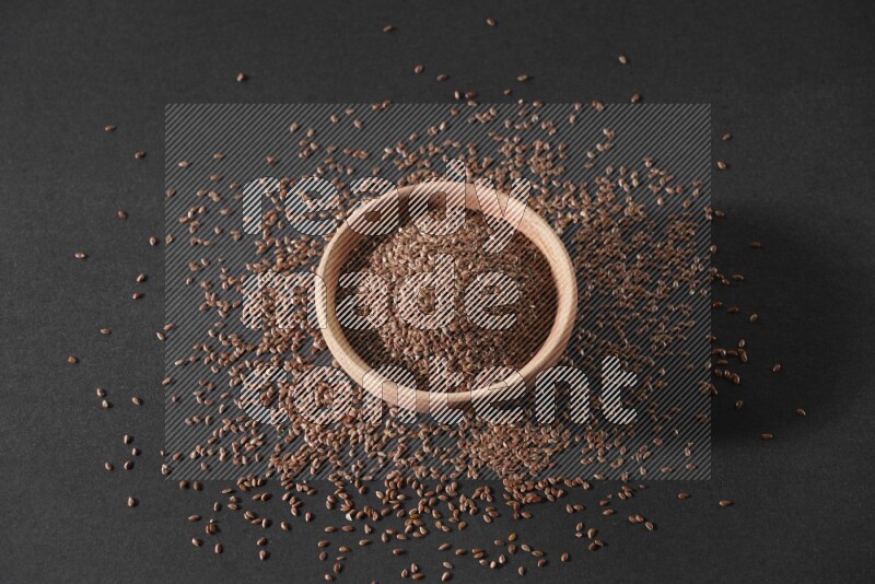 A wooden bowl full of flax surrounded by the seeds on a black flooring in different angles