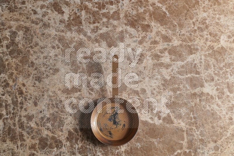 A small copper pan on beige marble background