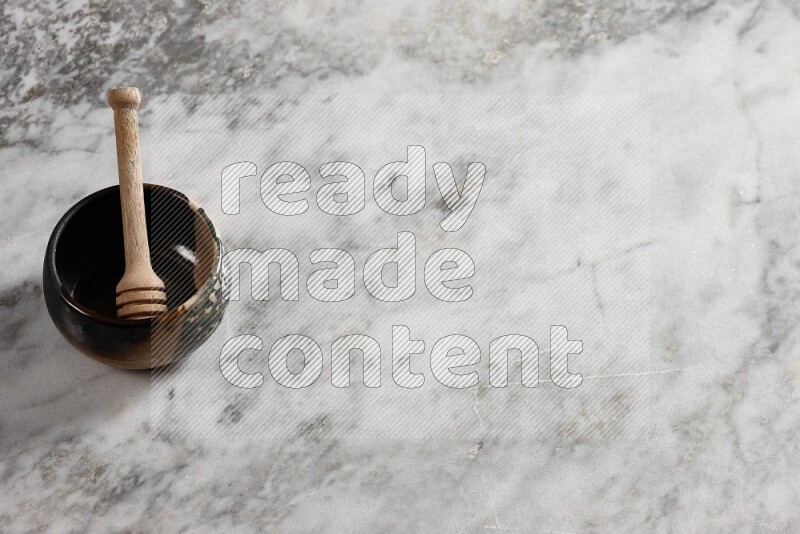 Multicolored pottery bowl with wooden honey dipper in it on grey marble background