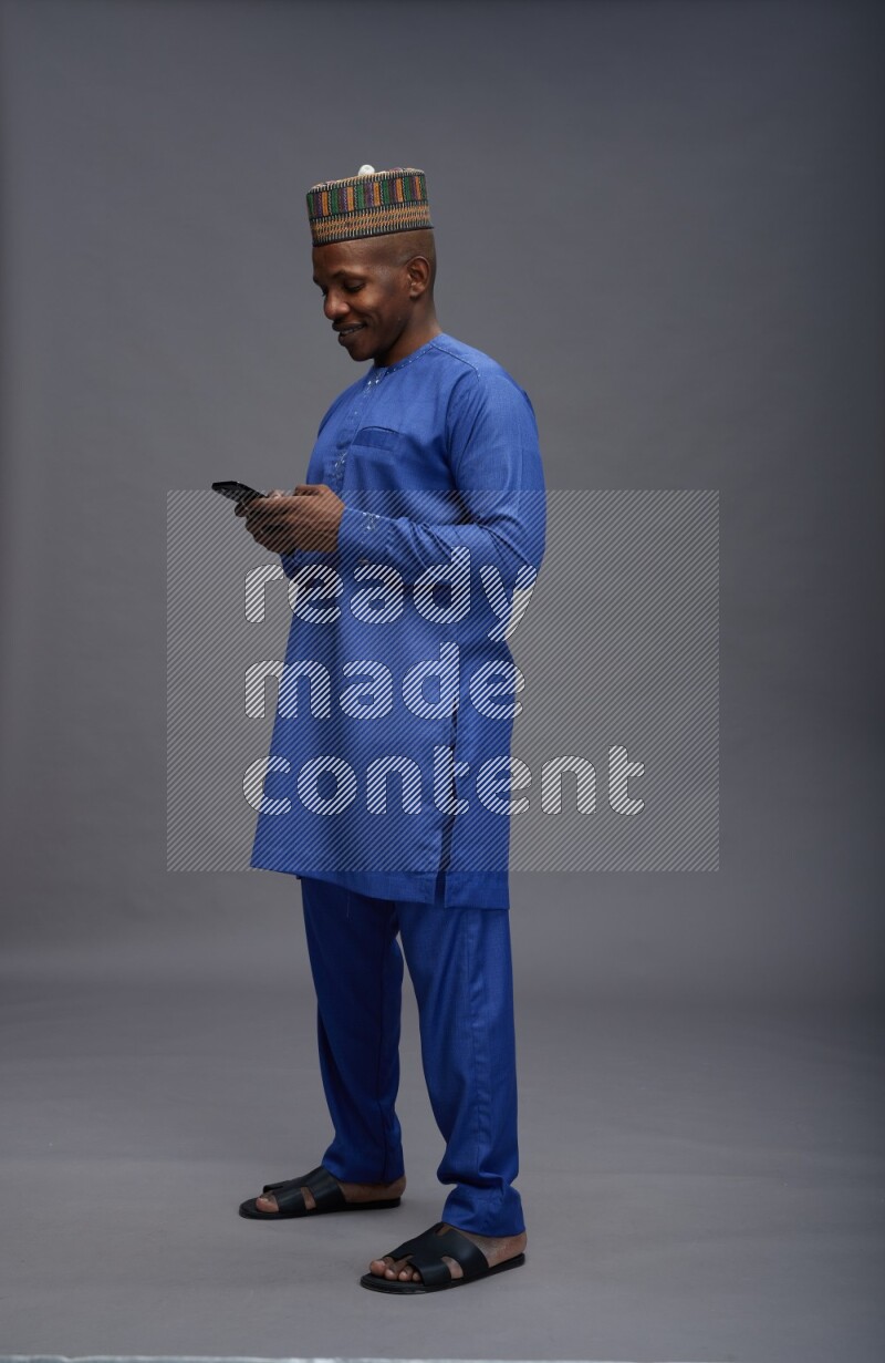 Man wearing Nigerian outfit standing texting on phone on gray background