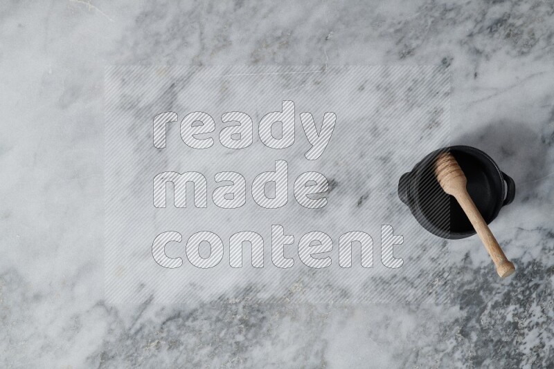 Black pottery bowl with wooden honey dipper in it on grey marble background