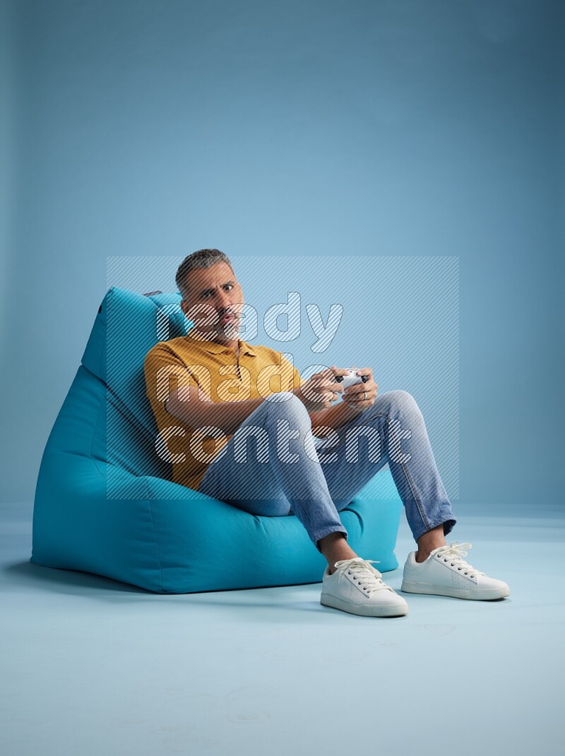 A man sitting on a blue beanbag and gaming with joystick