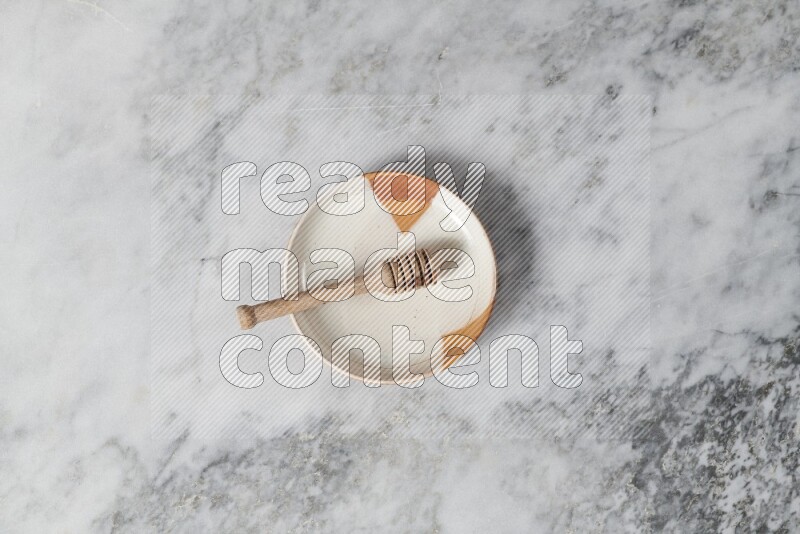Multicolored pottery plate with wooden honey dipper in it on grey marble background
