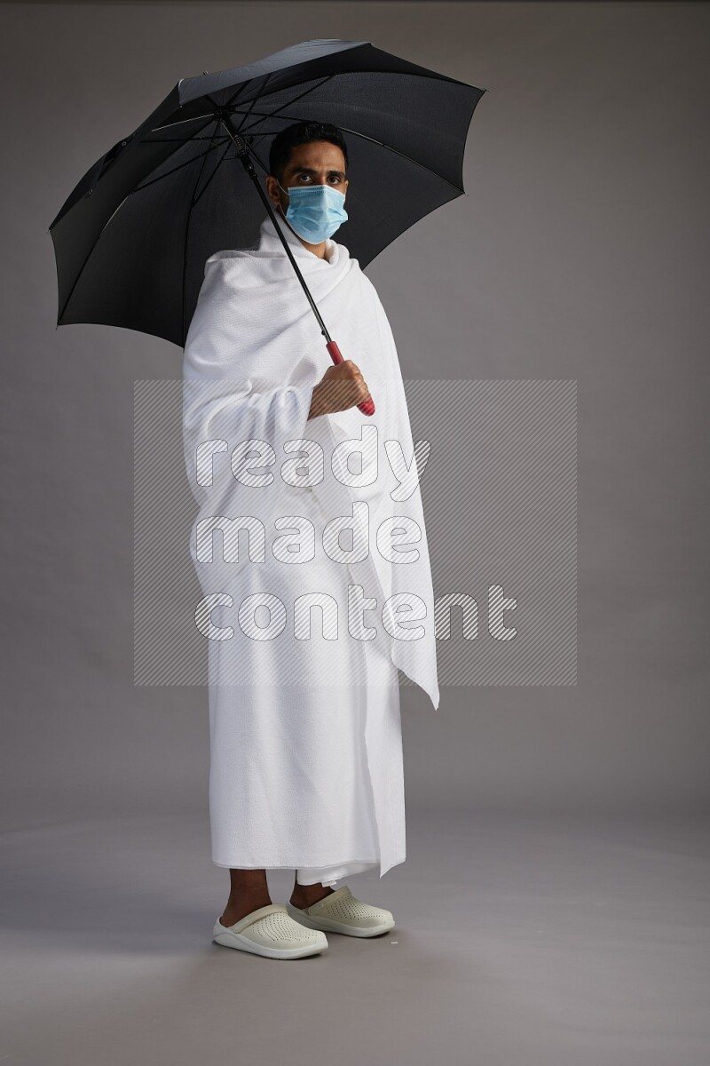 A man wearing Ehram and mask Standing holding umbrella on gray background on gray background