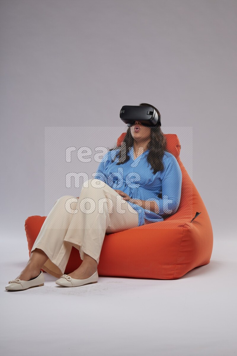 A woman sitting on an orange beanbag and gaming with VR