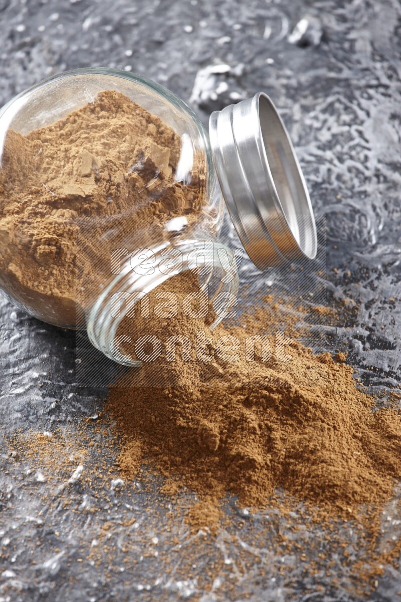 Flipped herbal glass jar full of cinnamon powder on textured black background