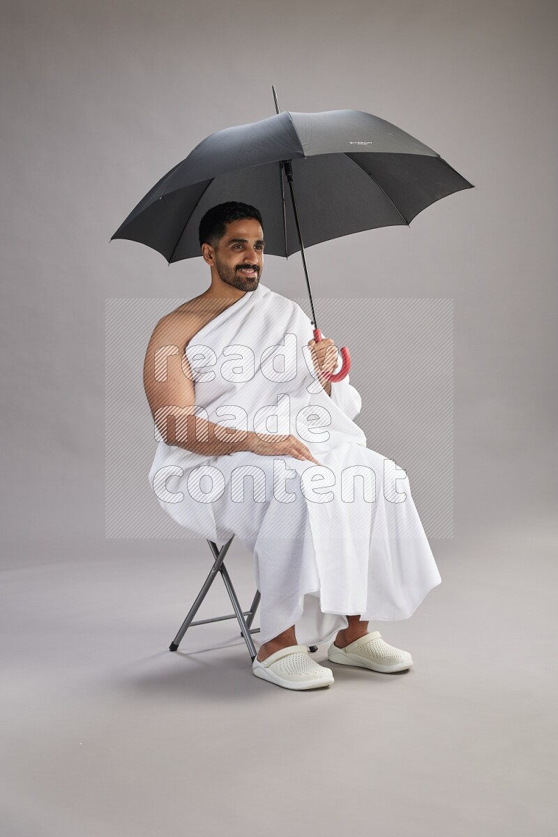 A man wearing Ehram with face mask Standing holding umbrella on gray background