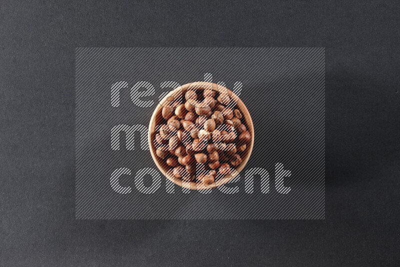 A wooden bowl full of peeled hazelnuts on a black background in different angles