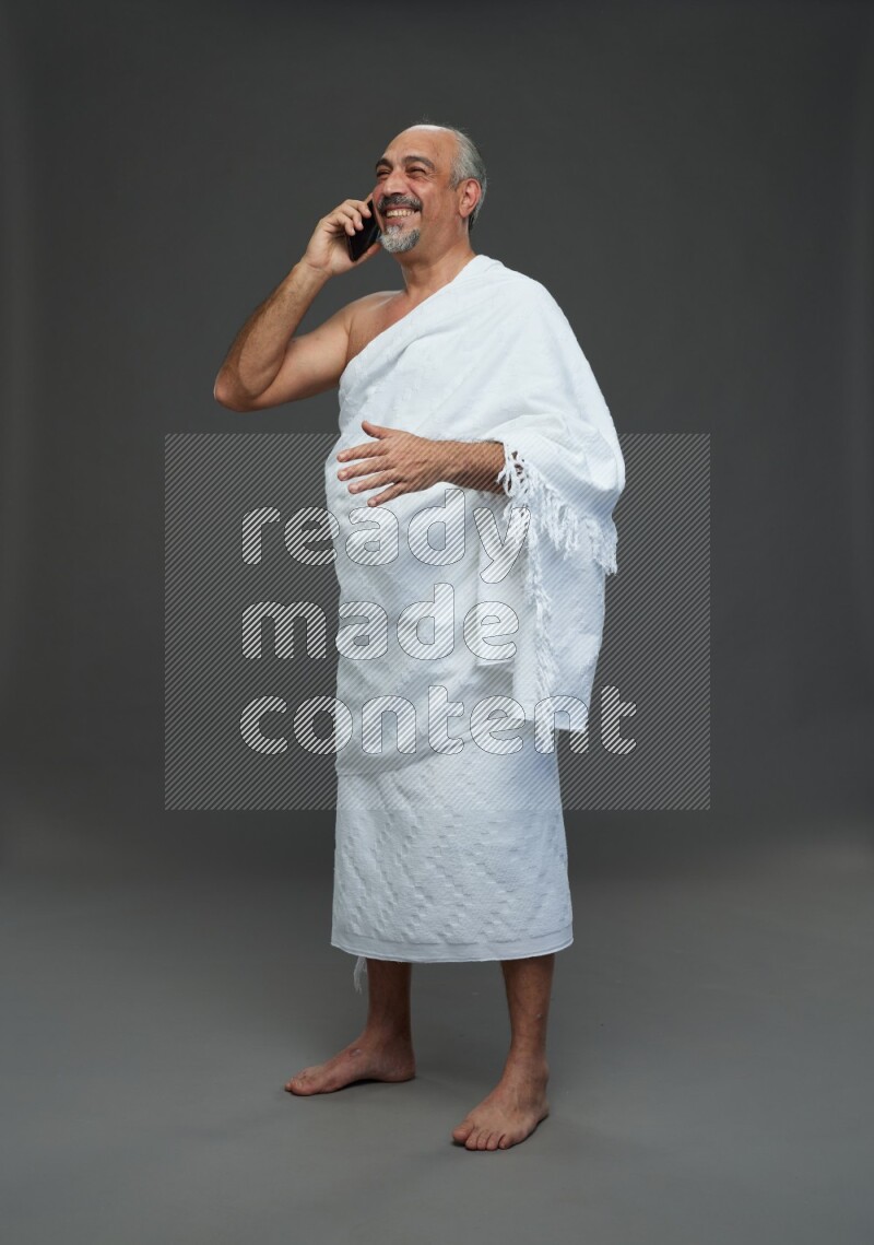 A man wearing Ehram Standing talking on phone on gray background