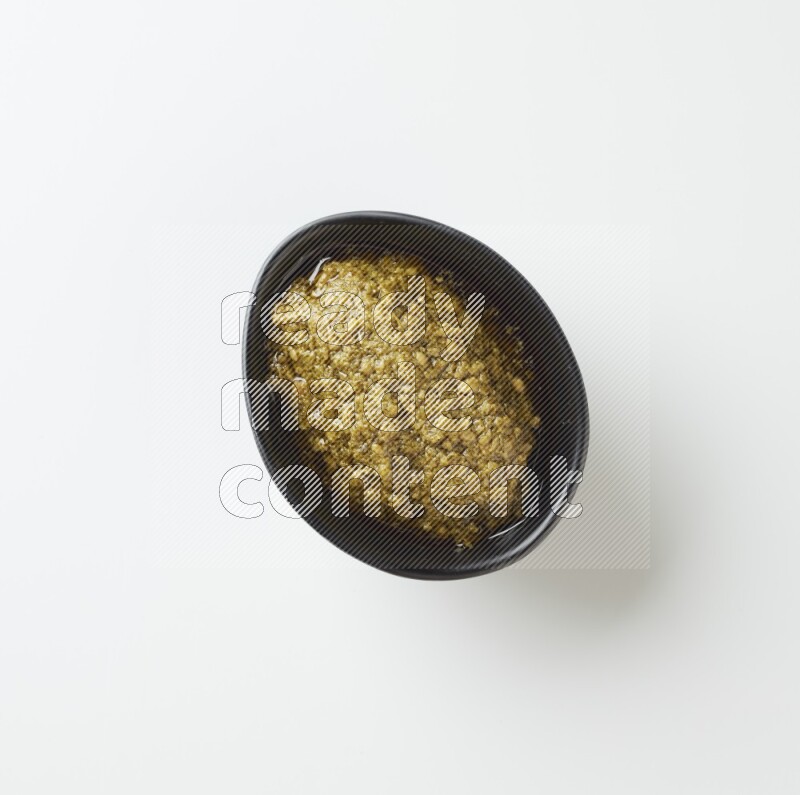 Medium oval black ceramic bowl filled with pesto paste on a white table top