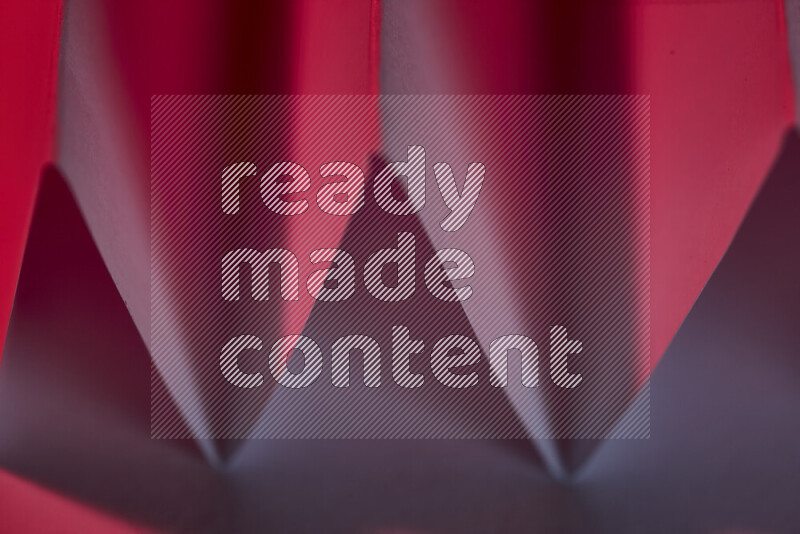 A close-up abstract image showing sharp geometric paper folds in red gradients
